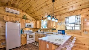 Una cocina estilo cabaña con paredes de madera, una isla central, electrodomésticos blancos y una lámpara colgante.
