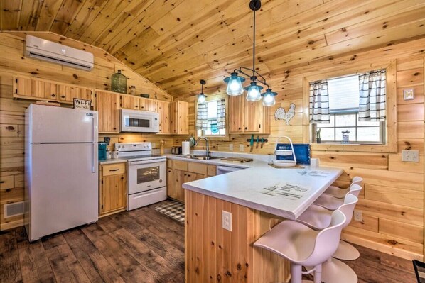 A cabin-style kitchen with wooden walls, a central island, white appliances, and a hanging light fixture.