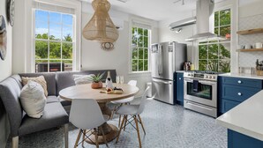 A modern kitchen with a dining area, large windows, and a view of greenery.
