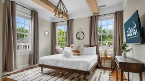 A bedroom with a large bed, wooden beams, a TV, and a view of greenery outside.