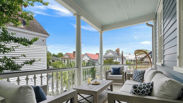 A covered porch with outdoor furniture, including a sofa and chairs, and a table with a drink.