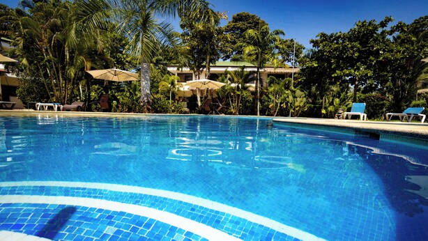 A clear blue pool surrounded by palm trees and lounge chairs. - Condo Pacifico Quepos, 5 minutes from National Park Manuel Antonio (Quepos)