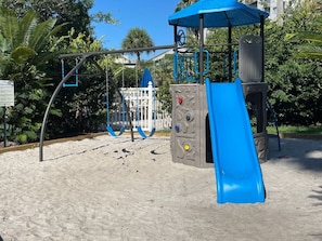 Kids can play on the playground's slide and climbing structures surrounded by sand.