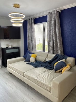 Relax in this stylish living room with a comfortable sofa, mounted TV, and large window with patterned curtains.