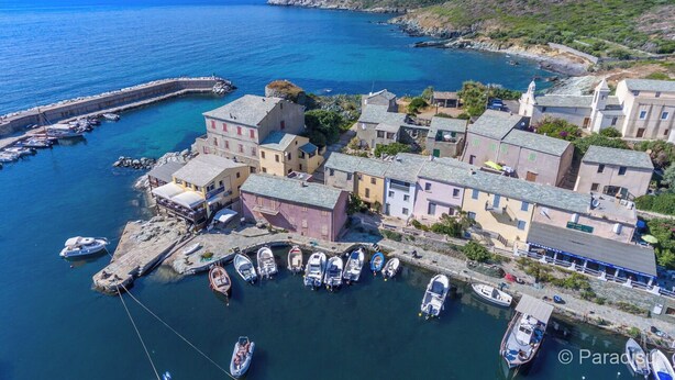A coastal village with traditional buildings, a marina with boats, and a rocky coastline.
