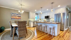 A modern kitchen with white cabinets, stainless steel appliances, and a central island with bar stools. - New Bern Waterfront Sunset (New Bern)