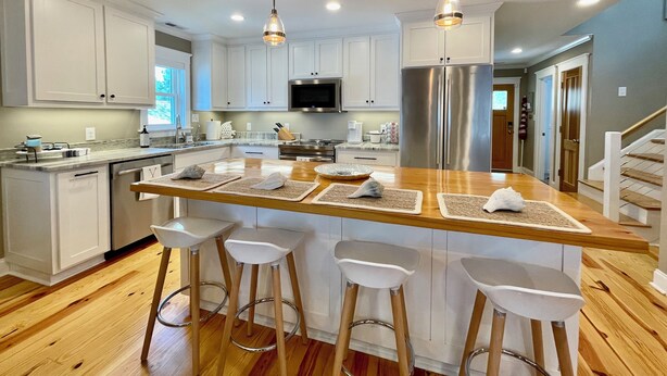 A modern kitchen with white cabinets, stainless steel appliances, and a wooden island with bar stools. - New Bern Waterfront Sunset (New Bern)