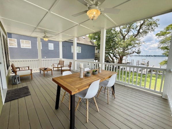 A covered outdoor deck with a wooden table and chairs, a ceiling fan, and a view of a lake. - New Bern Waterfront Sunset (New Bern)
