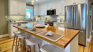 A modern kitchen with white cabinets, stainless steel appliances, and a wooden island with bar stools. - New Bern Waterfront Sunset (New Bern)