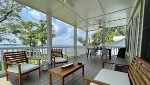 A covered outdoor deck with wooden furniture, a table, and chairs, overlooking a body of water. - New Bern Waterfront Sunset (New Bern)