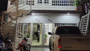 Un edificio de dos pisos con una escalera espiral, un coche en la entrada y una motocicleta adelante.