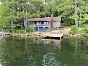 Enjoy serene lake views from the porch of this cabin-style house surrounded by lush greenery and trees.