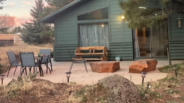 A rustic cabin with a covered patio, outdoor seating, and a large window. - Cottage with a stone fire pit and pet friendly! (Flagstaff)