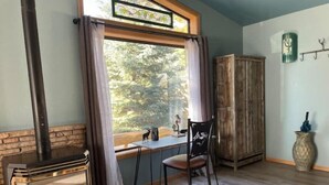 A cozy room with a fireplace, a window with curtains, a wooden cabinet, and a chair. - Cottage with a stone fire pit and pet friendly! (Flagstaff)