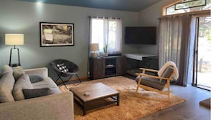 A living room with a sofa, a rocking chair, a coffee table, a TV, and a fireplace. - Cottage with a stone fire pit and pet friendly! (Flagstaff)
