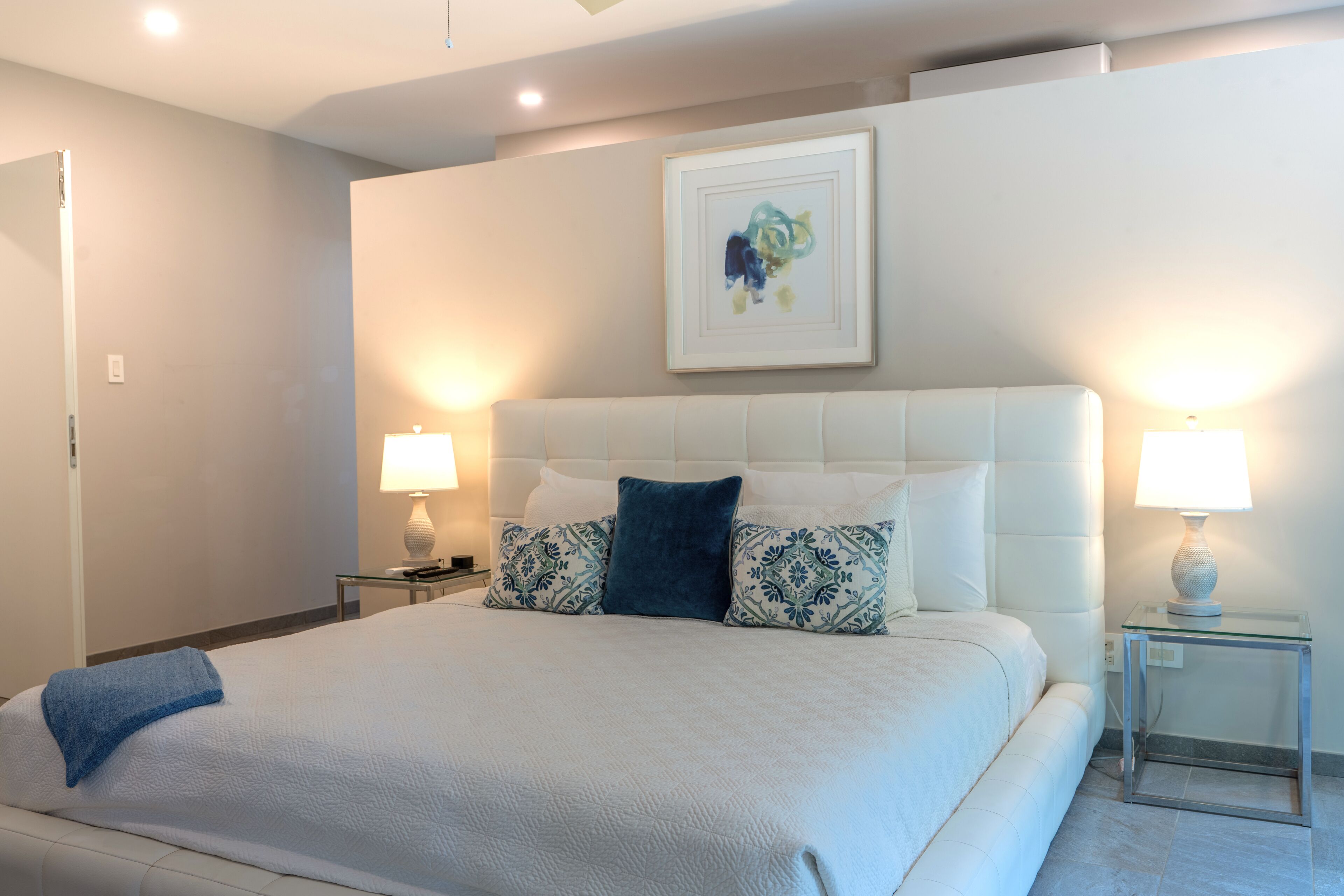 Una habitació d'hotel amb un llit gran, dues làmpades laterals, una obra d'art emmarcada a la paret i una taula auxiliar de vidre.