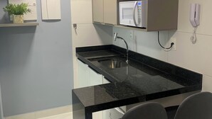 A modern kitchen with a black countertop, stainless steel sink, and two bar stools. - Melhores Flats (João Pessoa)