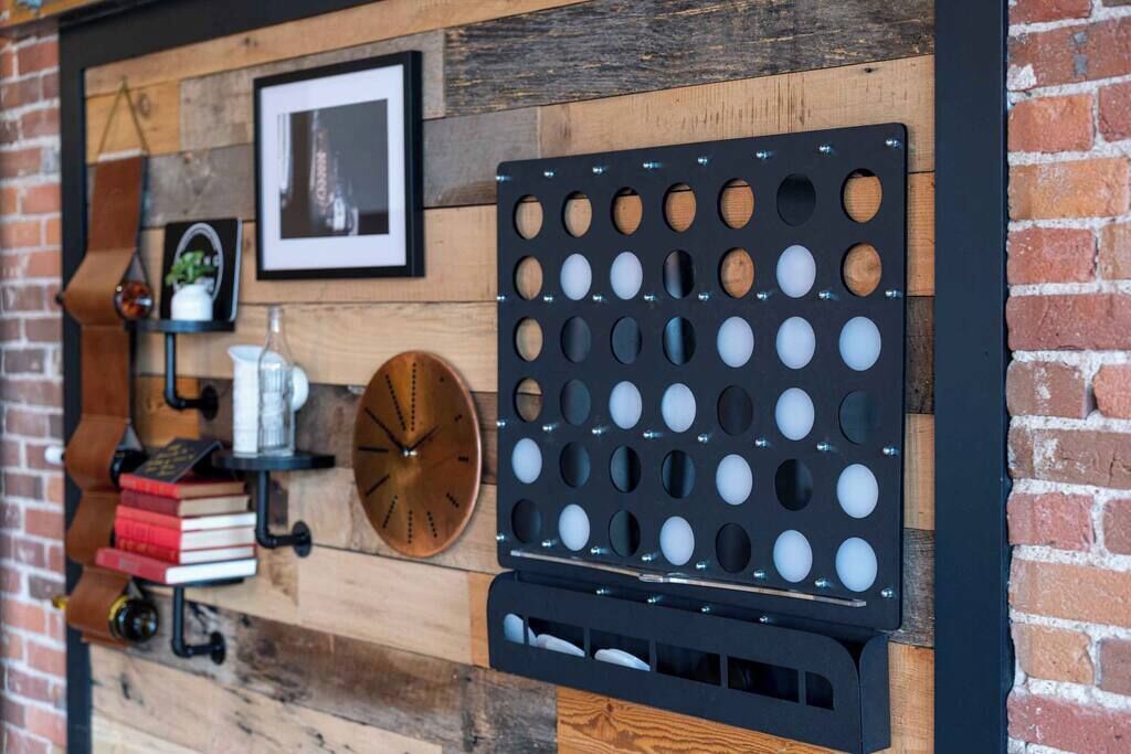A wall with a wooden panel design, a black metal object with circular cutouts, a clock, and a shelf with books and a plant.