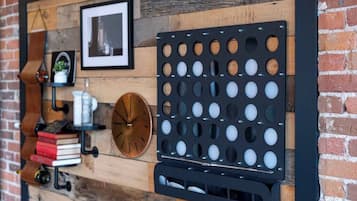 A wall with a wooden panel design, a black metal object with circular cutouts, a clock, and a shelf with books and a plant.