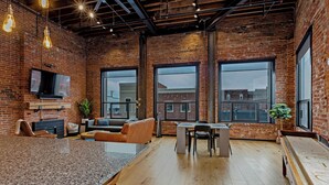 A spacious room with a large granite countertop, a television mounted on the brick wall, and a seating area with a sofa and chairs. - The Exchange. Big Luxury Loft, XCHNG. Modern Loft in the heart of Effingham.  (Effingham)