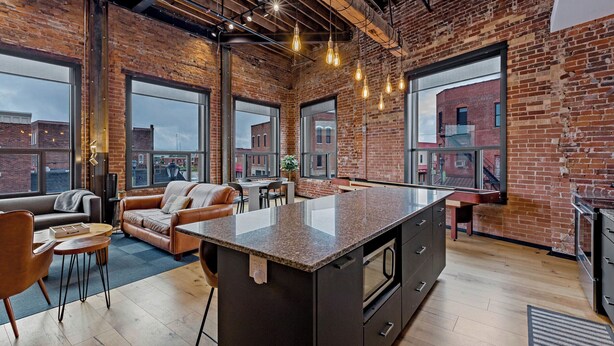 A spacious kitchen with a large island, exposed brick walls, and large windows offering views of the city. - The Exchange. Big Luxury Loft, XCHNG. Modern Loft in the heart of Effingham.  (Effingham)