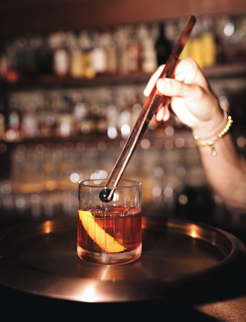 A hand holding a cocktail glass with a straw, placed on a tray.