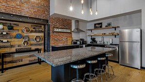 Eine moderne Küche mit einer zentralen Kochinsel, Barhocker, einem Edelstahlkühlschrank und einer Wand mit Ziegeln.