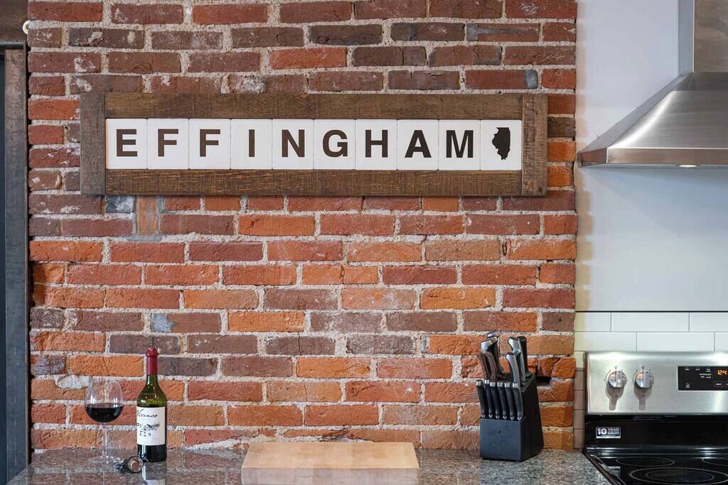 Ett kök med en tegelvägg, en skylt med texten ”EFFINGHAM”, en vinflaska och ett knivställ.