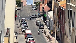 Una calle estrecha con coches aparcados y algunos peatones.