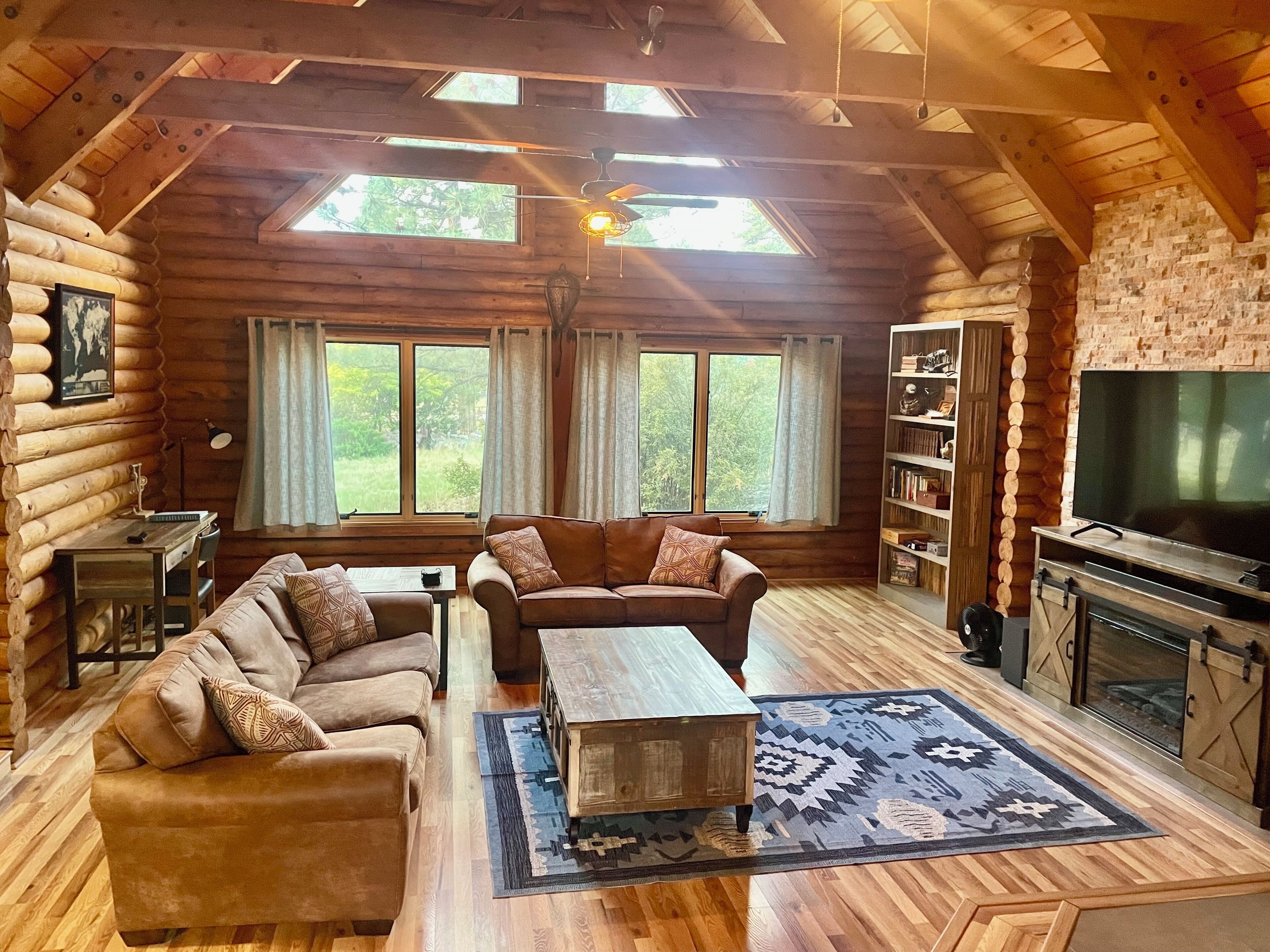 A log cabin interior with a wooden floor, a sofa, a coffee table, a fireplace, and a television.