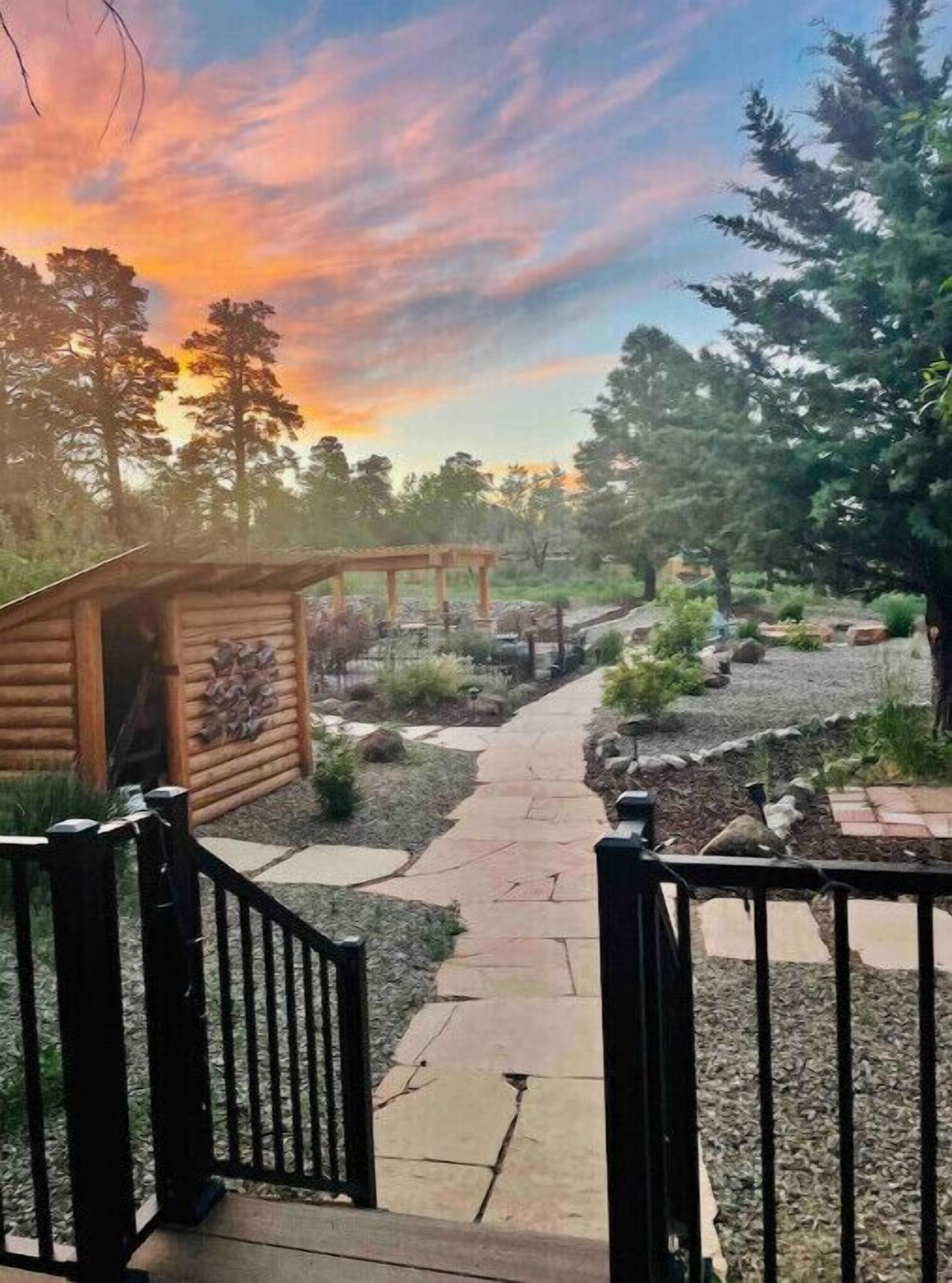 A wooden cabin with a stone pathway leading to it, surrounded by trees and a clear sky.