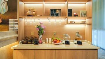 A hotel reception area with a wooden counter, a vase of flowers, a coffee machine, and a fruit bowl.