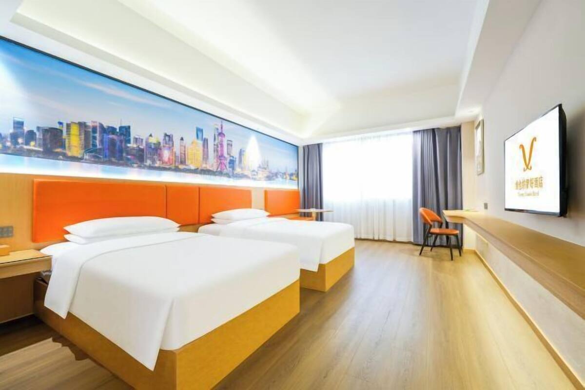 A hotel room with two beds, a cityscape mural, a TV, and a desk with a chair.