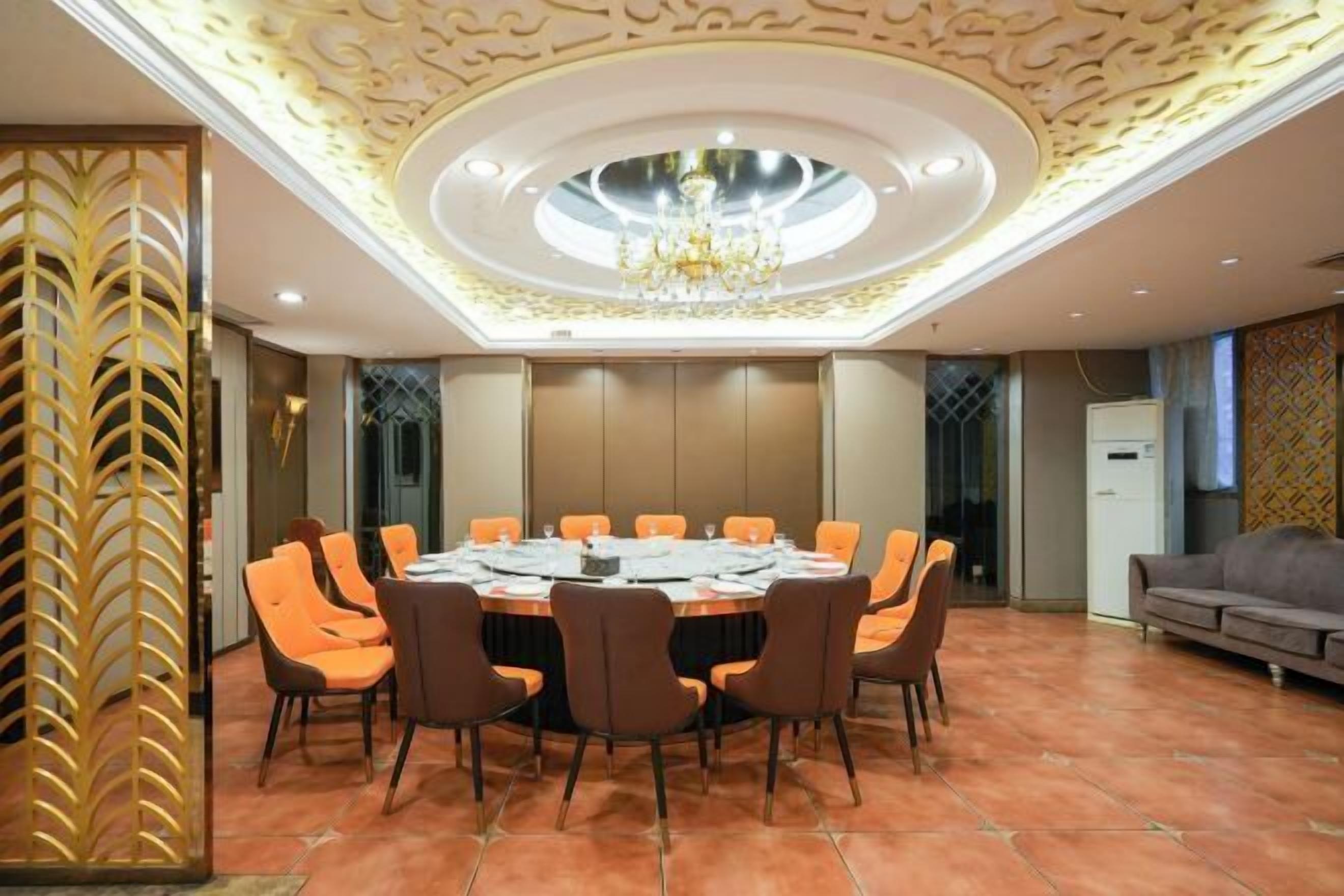 A conference room with a round table, orange chairs, a chandelier, and a decorative ceiling.