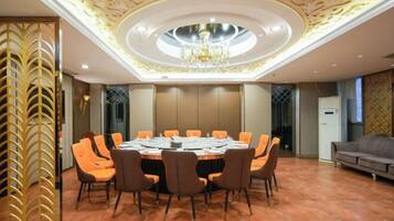 A conference room with a round table, orange chairs, a chandelier, and a decorative ceiling.