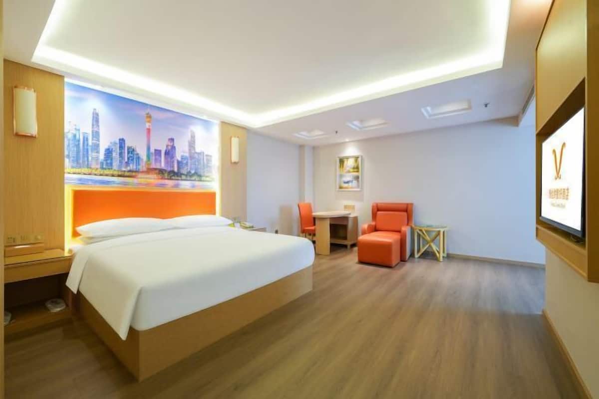 A hotel room with a bed, a desk, a chair, and a cityscape mural on the wall.