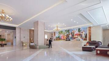 A spacious lobby with a marble floor, a reception desk, a large mural, and a chandelier.