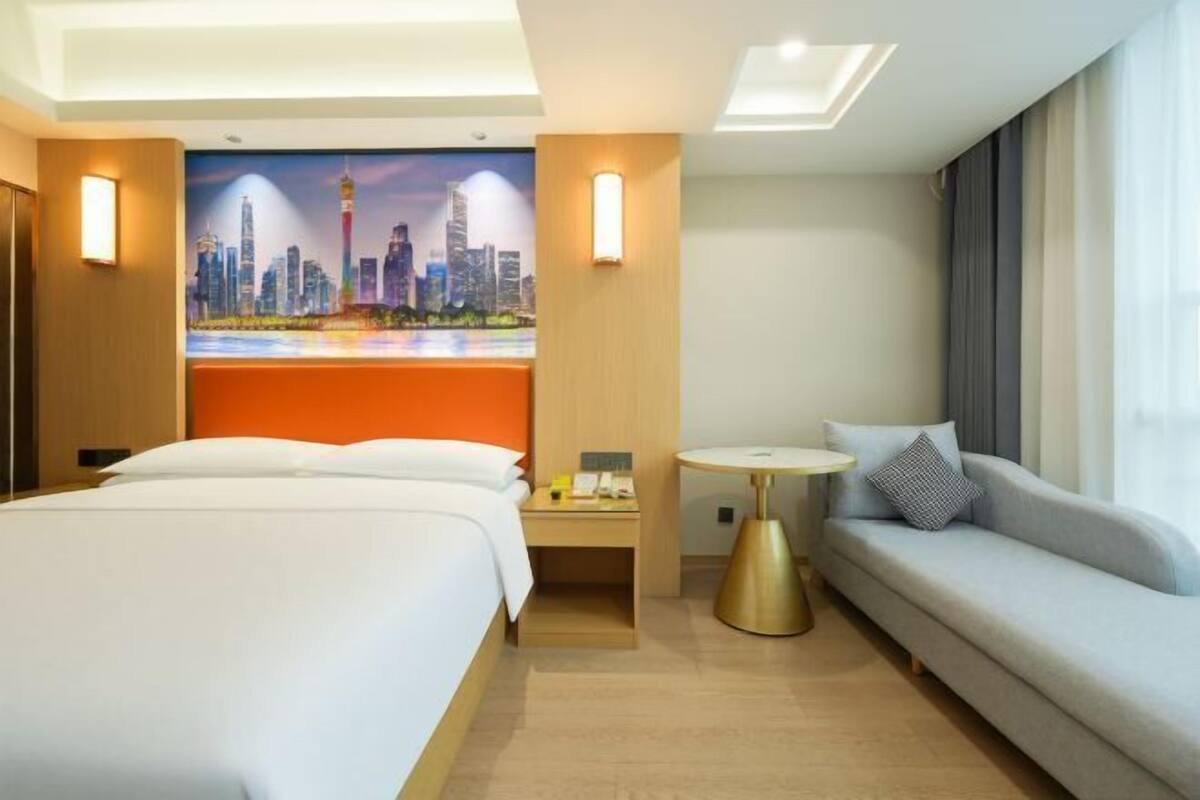 A hotel room with a bed, a sofa, a small table, a nightstand, and a cityscape mural on the wall.