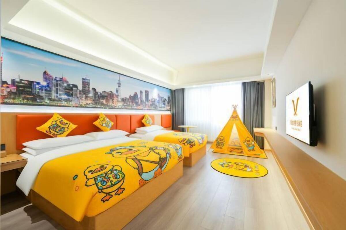 A hotel room with two beds, a cityscape mural, a television, and a tent decoration.