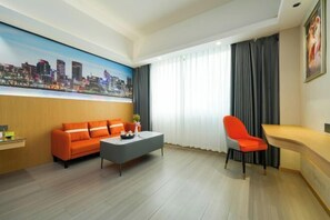 A modern hotel room with a cityscape painting, a sofa, a coffee table, a desk, and a chair.