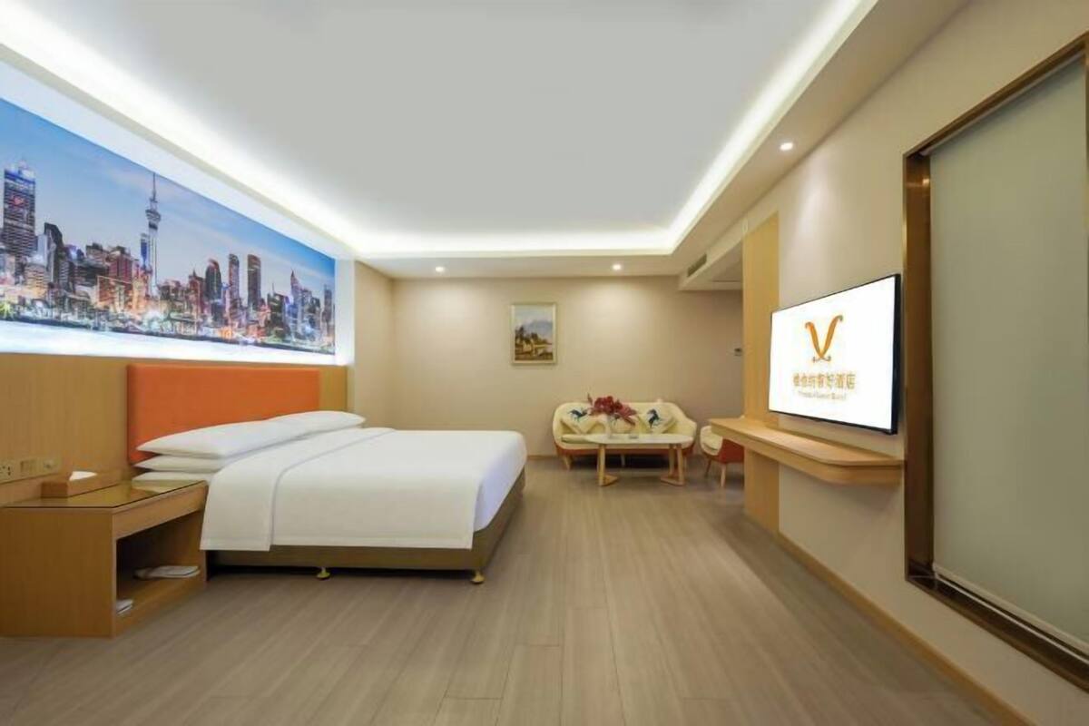 A hotel room with a bed, a desk, a TV, and a painting of a cityscape.
