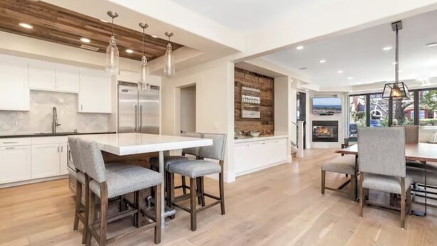Une cuisine moderne avec des meubles blancs, un grand îlot central et des tabourets de bar. On y trouve également un coin repas avec une table et des chaises.