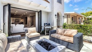 Une terrasse extérieure aménagée avec des meubles en osier, un barbecue et un foyer.