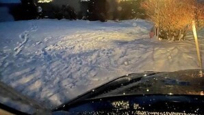 Une maison dont le toit est recouvert de neige et dont la fenêtre est illuminée d’une lumière verte.