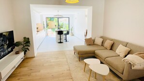 A modern living room with a sofa, a TV, and a dining area visible through an open door. - Modern townhouse - Private Garden (Differdange)