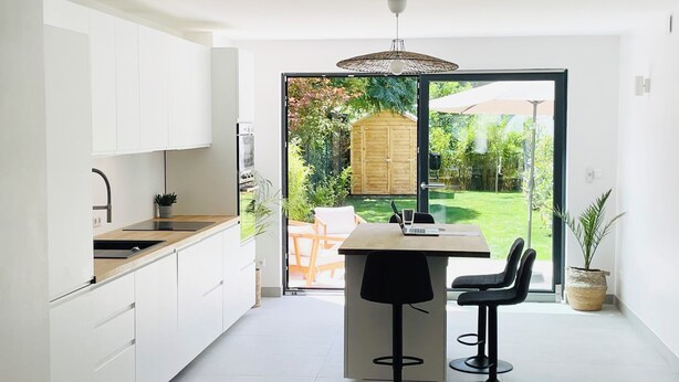 A modern kitchen with white cabinets, a wooden countertop, and a large sliding glass door leading to a garden. - Modern townhouse - Private Garden (Differdange)