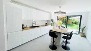 A modern kitchen with white cabinets, a wooden countertop, a sink, and a dining area with two black bar stools. - Modern townhouse - Private Garden (Differdange)
