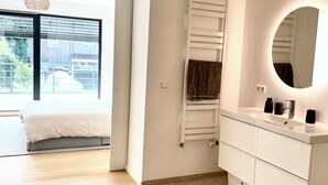 A modern bedroom with a large bed, a walk-in closet, and a bathroom with a vanity and mirror. - Modern townhouse - Private Garden (Differdange)