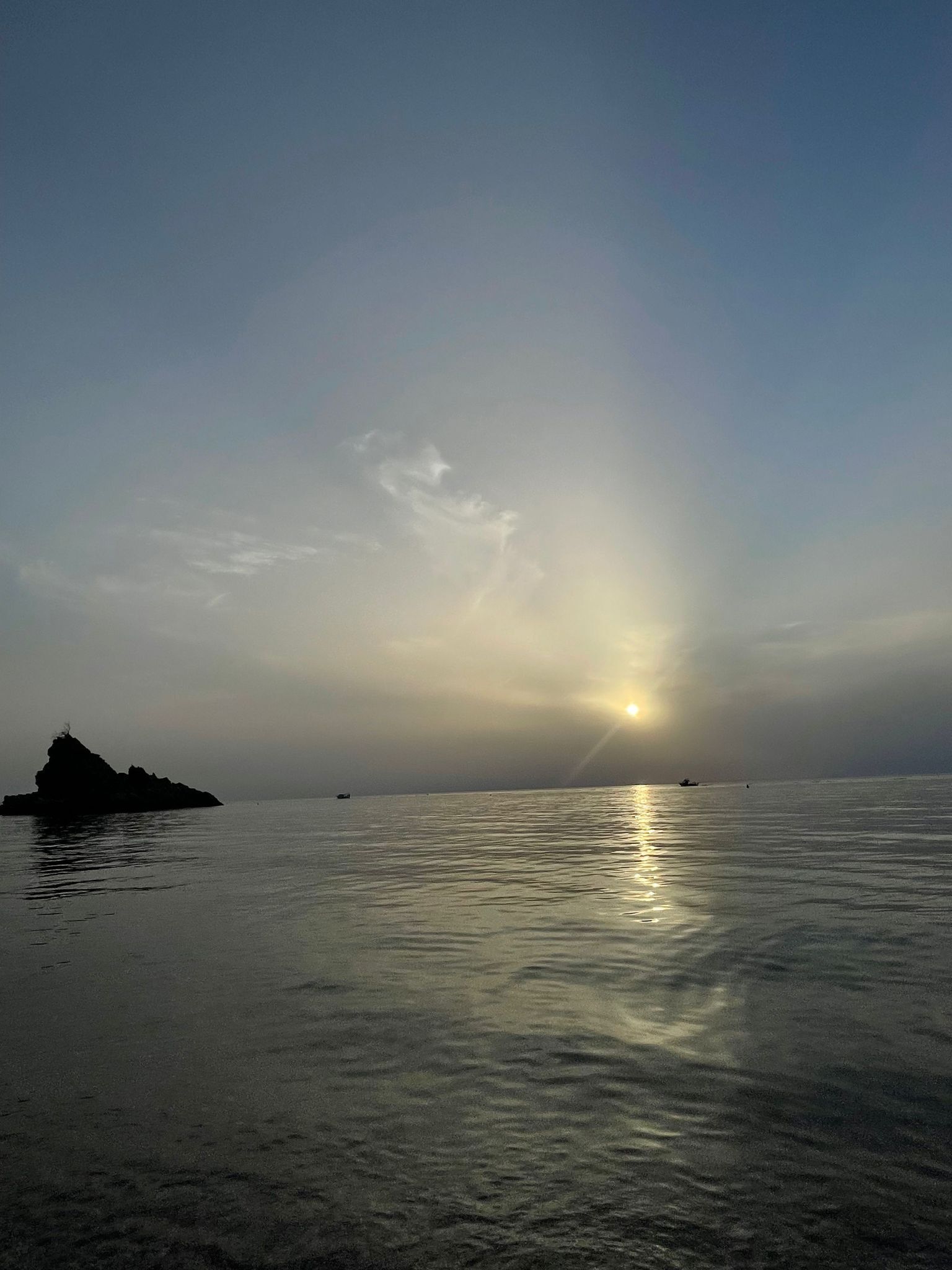 Mar tranquila con una pequeña isla y el sol poniéndose o saliendo.
