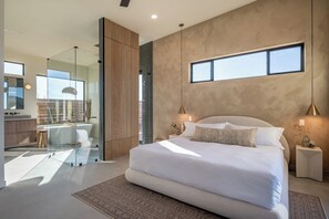 A modern bedroom with a large bed, a glass shower enclosure, and a view of the outside.